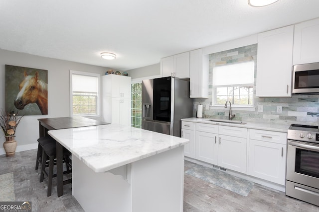 kitchen with a kitchen island, light stone countertops, a sink, white cabinets, and stainless steel appliances