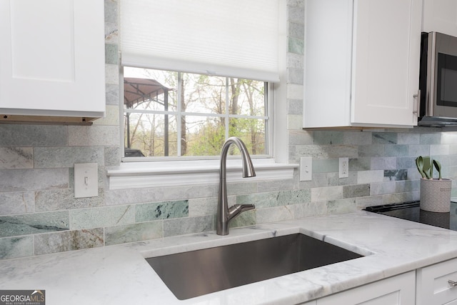 kitchen with decorative backsplash, light stone countertops, a sink, stainless steel microwave, and white cabinetry