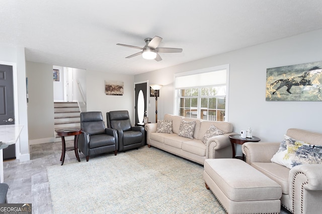 living area with baseboards, ceiling fan, and stairs
