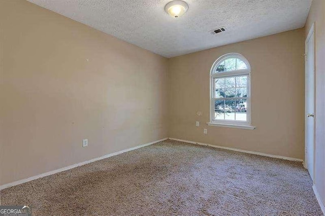 spare room with visible vents, a textured ceiling, carpet floors, and baseboards