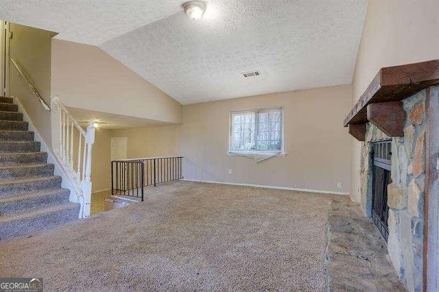 unfurnished living room featuring a textured ceiling, vaulted ceiling, a stone fireplace, and visible vents
