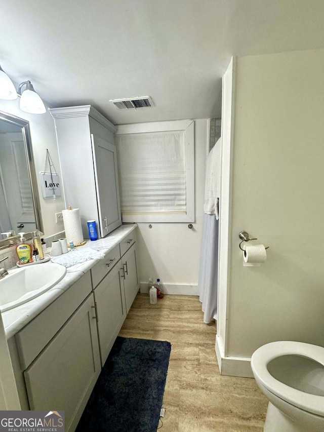bathroom with vanity, toilet, baseboards, wood finished floors, and visible vents