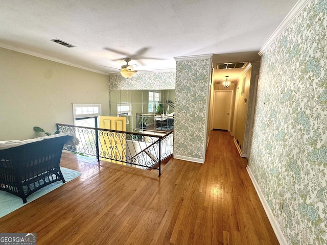 corridor featuring visible vents, crown molding, wood finished floors, and wallpapered walls