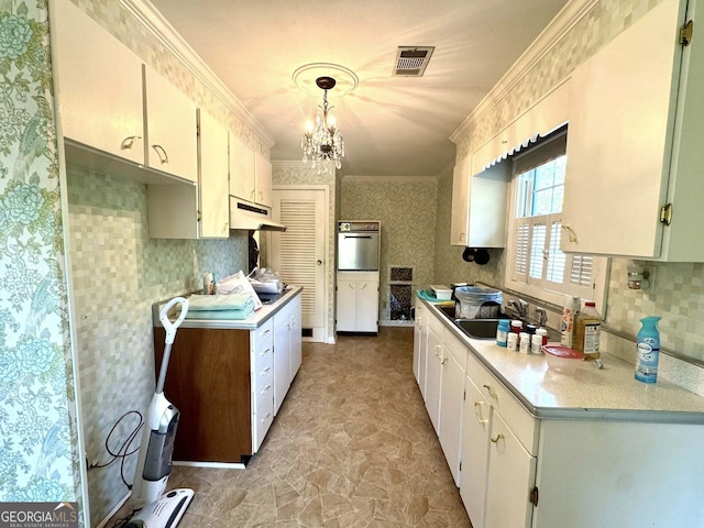 kitchen with visible vents, a sink, ornamental molding, under cabinet range hood, and oven