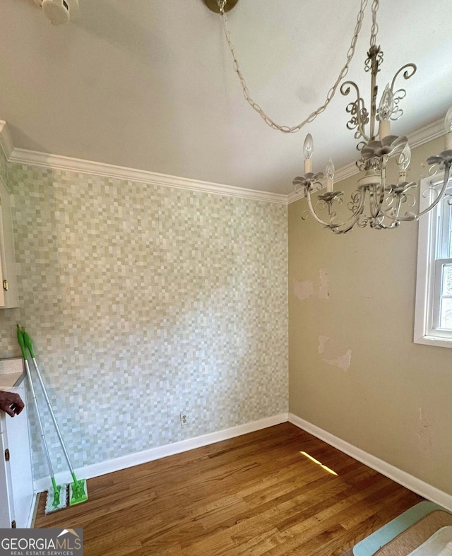 unfurnished dining area featuring baseboards, an inviting chandelier, ornamental molding, and wood finished floors