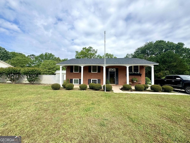 view of front of home with covered porch, brick siding, fence, and a front lawn
