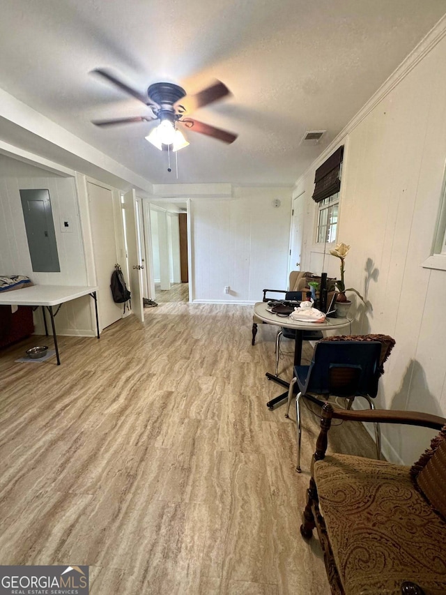 interior space with ceiling fan, electric panel, wood finished floors, and visible vents