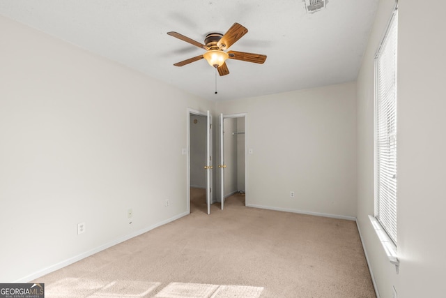 unfurnished bedroom featuring visible vents, baseboards, light colored carpet, a spacious closet, and a ceiling fan
