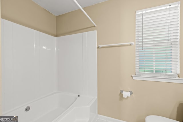 bathroom featuring baseboards, bathing tub / shower combination, and toilet