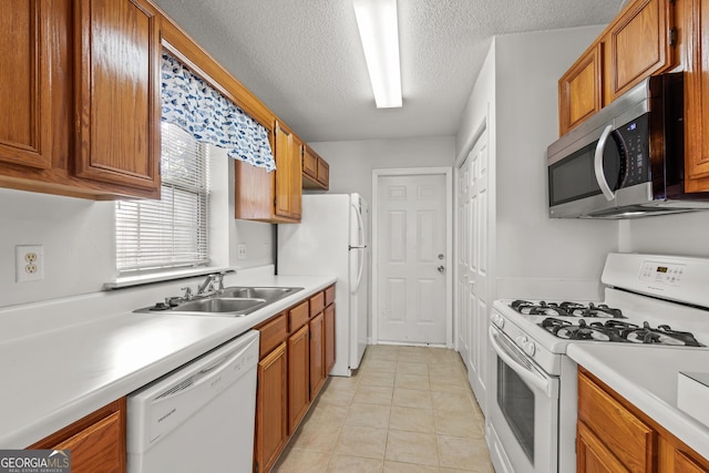 kitchen with brown cabinetry, a textured ceiling, a sink, light countertops, and white appliances