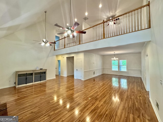 unfurnished living room featuring visible vents, wood finished floors, ceiling fan with notable chandelier, and a towering ceiling