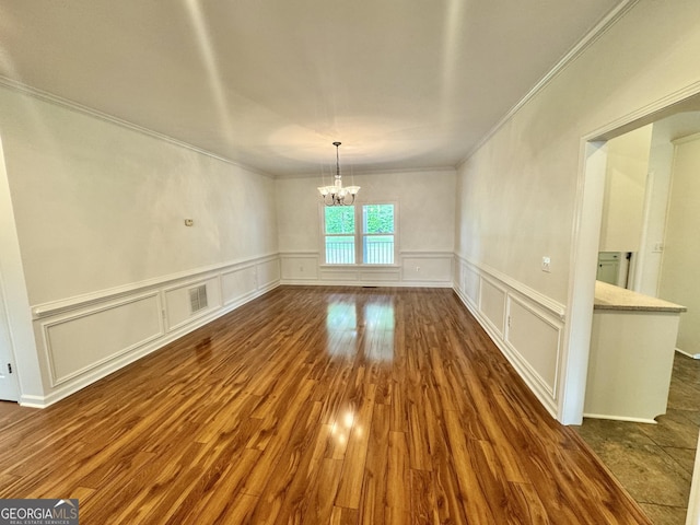 unfurnished dining area with ornamental molding, dark wood-style flooring, wainscoting, a decorative wall, and a notable chandelier