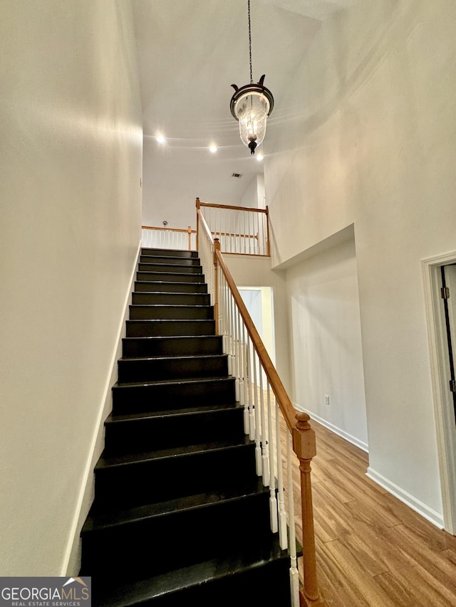 staircase featuring a high ceiling, a chandelier, recessed lighting, baseboards, and wood finished floors