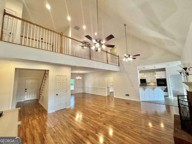 unfurnished living room with visible vents, wood finished floors, high vaulted ceiling, ceiling fan with notable chandelier, and stairs