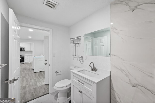 bathroom featuring washer / clothes dryer, toilet, vanity, decorative backsplash, and wood finished floors