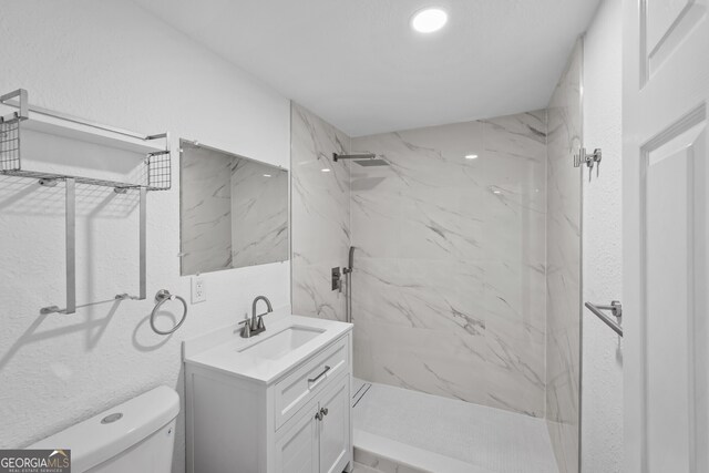 bathroom with a marble finish shower, vanity, and toilet
