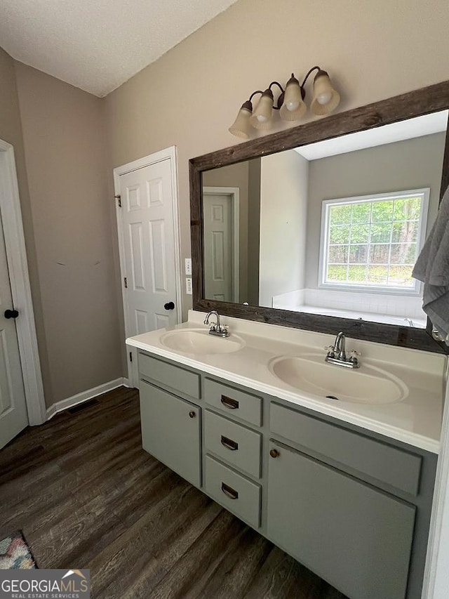 full bath with double vanity, a sink, baseboards, and wood finished floors