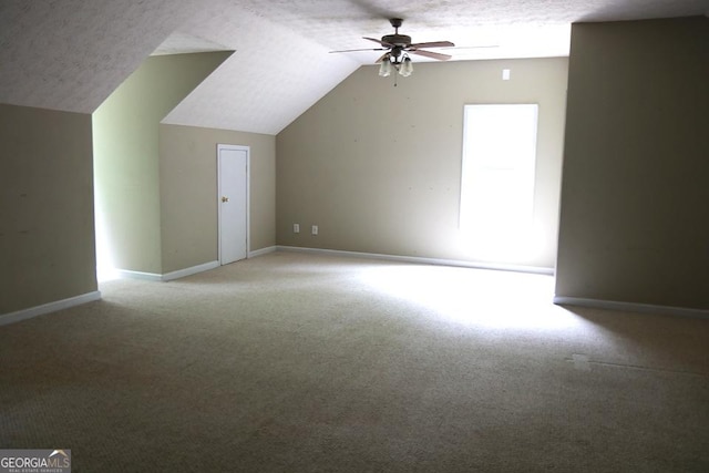additional living space featuring baseboards, light colored carpet, a textured ceiling, a ceiling fan, and vaulted ceiling