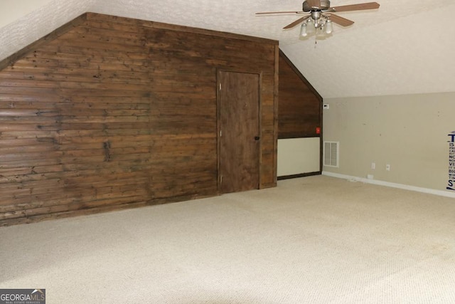 additional living space featuring ceiling fan, light carpet, wood walls, lofted ceiling, and visible vents