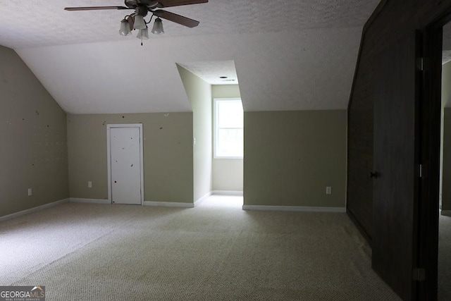 bonus room with light carpet, a textured ceiling, a ceiling fan, baseboards, and lofted ceiling