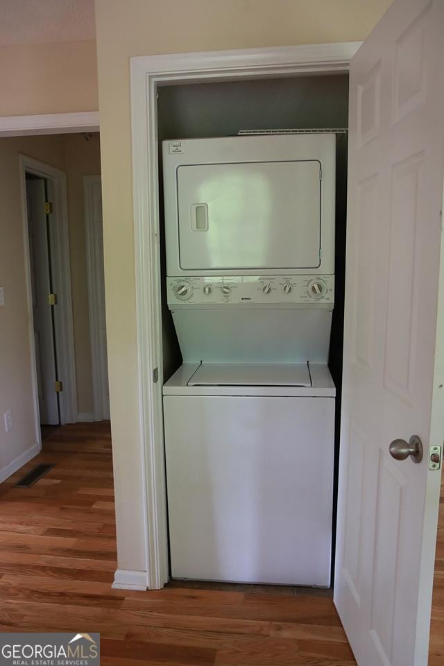 washroom featuring laundry area, wood finished floors, and stacked washer and clothes dryer