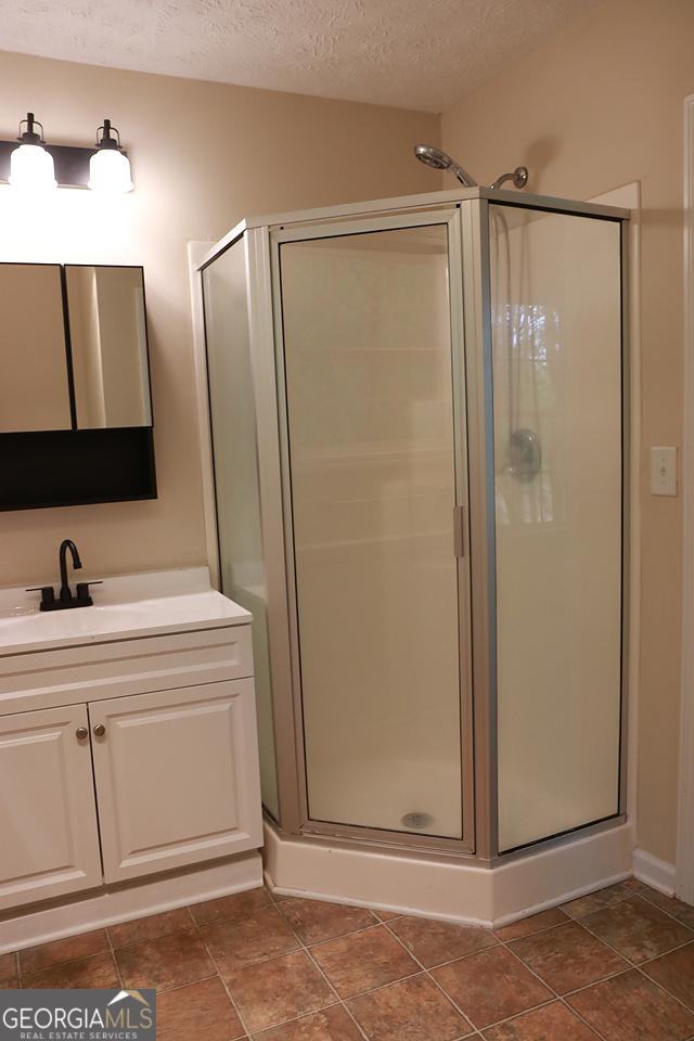 full bath featuring a textured ceiling, a shower stall, and vanity