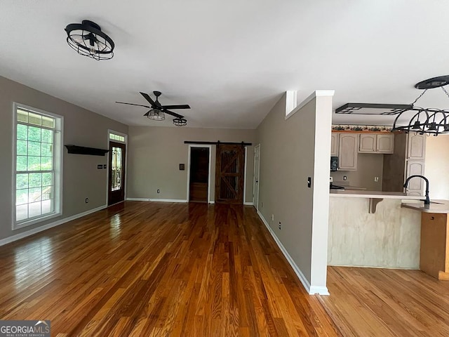 unfurnished living room with ceiling fan, a sink, a barn door, and wood finished floors
