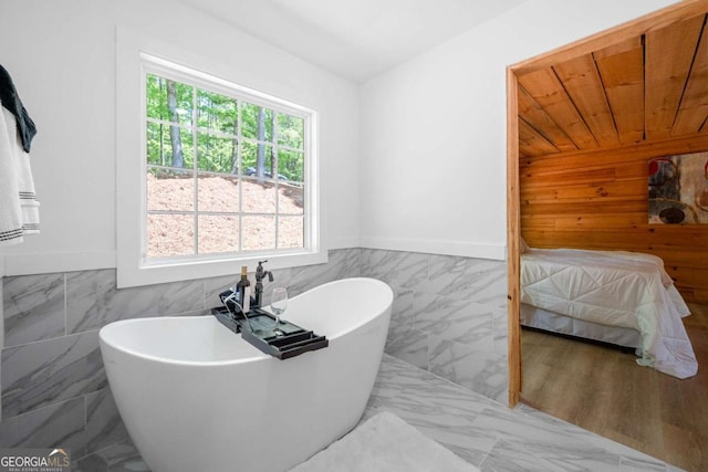 bathroom featuring a freestanding tub, tile walls, marble finish floor, and a wainscoted wall