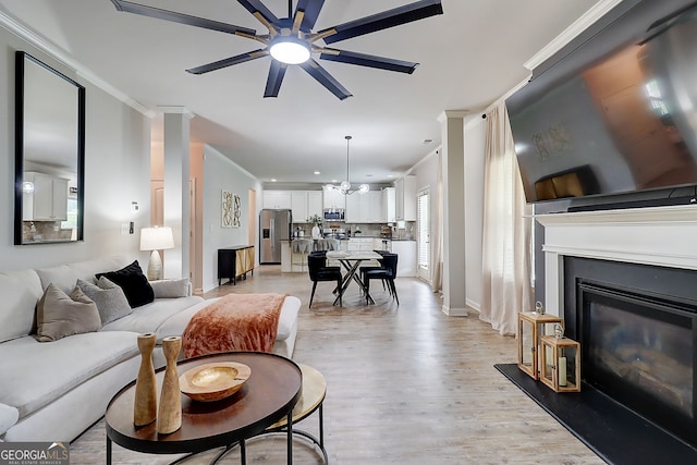 5601 Savannah River Rd, Atlanta, GA 30349 - living room featuring a glass covered fireplace, ceiling fan with notable chandelier, baseboards, light wood-type flooring, and ornamental molding