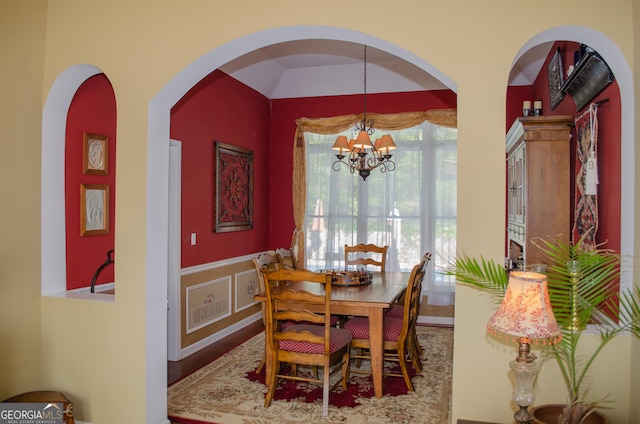 dining room featuring arched walkways, wainscoting, wood finished floors, and a notable chandelier