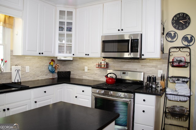 kitchen with dark countertops, appliances with stainless steel finishes, white cabinets, and glass insert cabinets