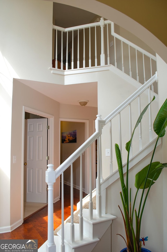 stairway with wood finished floors, baseboards, and a high ceiling