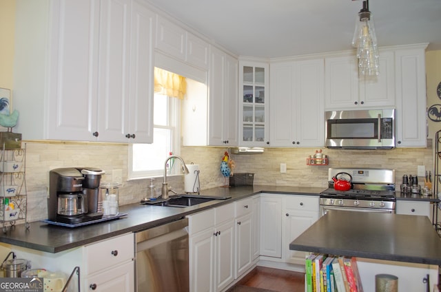 kitchen featuring white cabinets, stainless steel appliances, dark countertops, and a sink