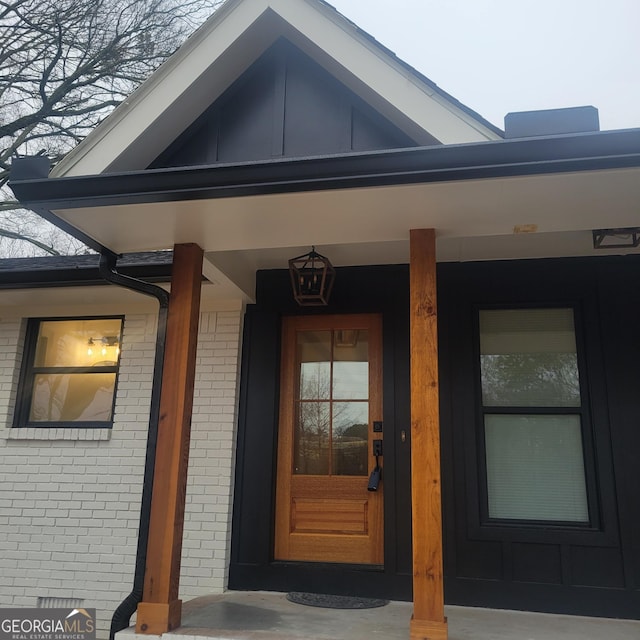 entrance to property featuring a porch, brick siding, and board and batten siding