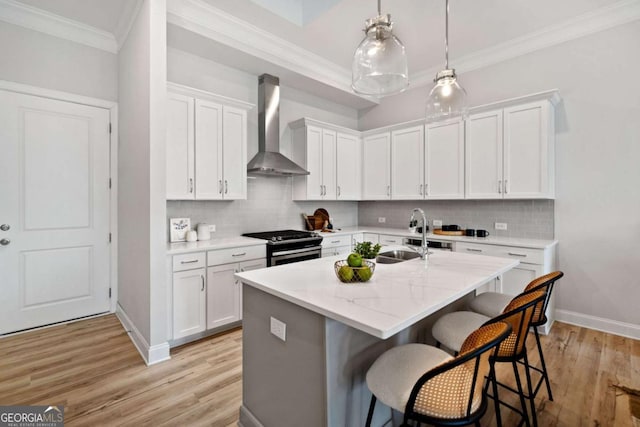 kitchen featuring crown molding, a sink, stainless steel gas stove, wall chimney exhaust hood, and a kitchen bar