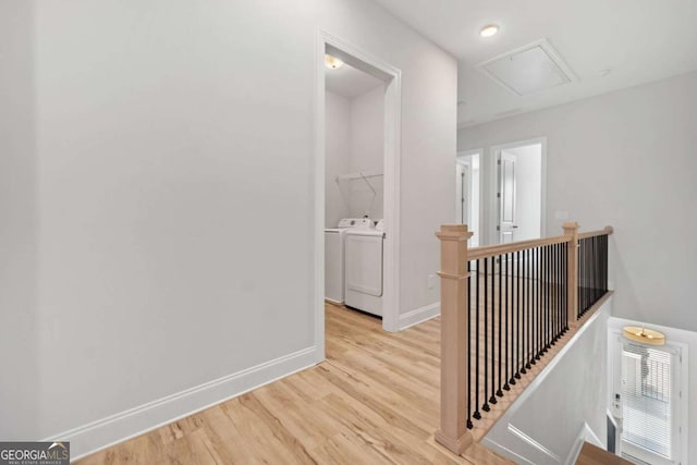 hallway featuring attic access, independent washer and dryer, wood finished floors, baseboards, and an upstairs landing