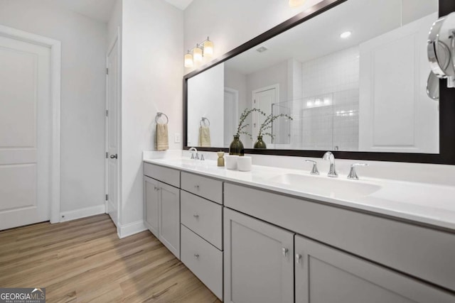 full bath featuring double vanity, a walk in shower, a sink, and wood finished floors