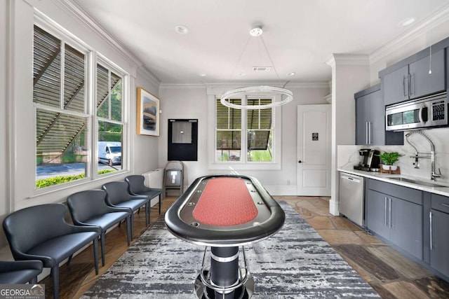 recreation room with plenty of natural light, a sink, crown molding, and stone tile flooring