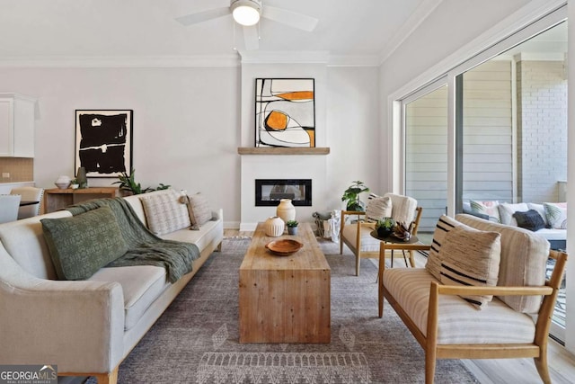 living area featuring crown molding, ceiling fan, a glass covered fireplace, and baseboards