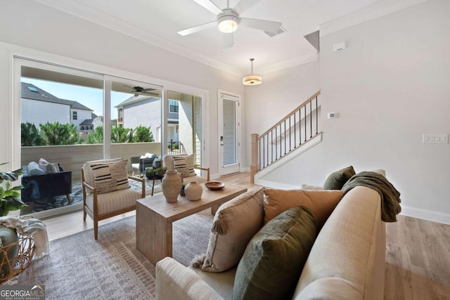 living area featuring crown molding, ceiling fan, light wood-style flooring, stairs, and baseboards