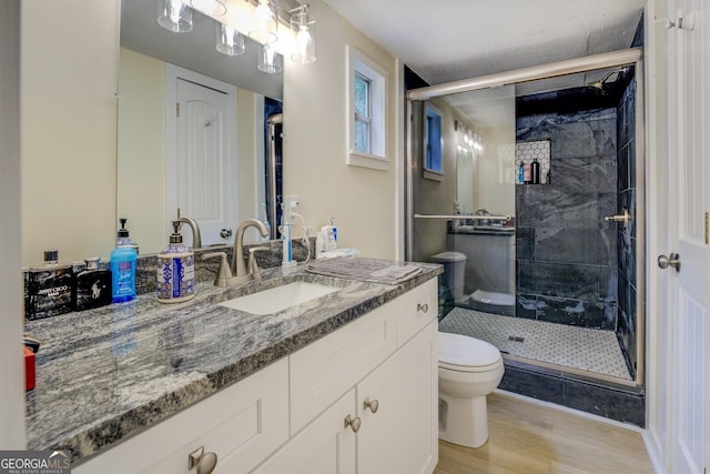 bathroom with wood finished floors, a stall shower, toilet, and vanity