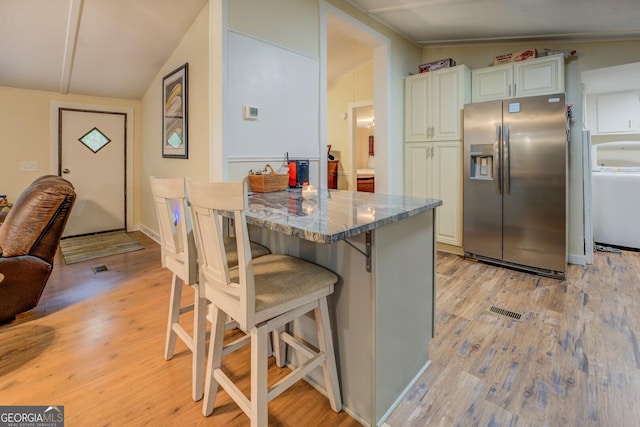 kitchen with stone countertops, washer / clothes dryer, a breakfast bar area, stainless steel fridge, and light wood-type flooring