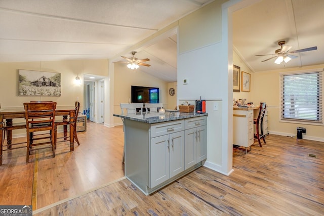 kitchen featuring a ceiling fan, baseboards, light wood-style floors, dark stone counters, and vaulted ceiling with beams