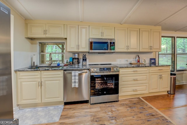 kitchen featuring a sink, stainless steel appliances, dark stone countertops, and light wood-style flooring