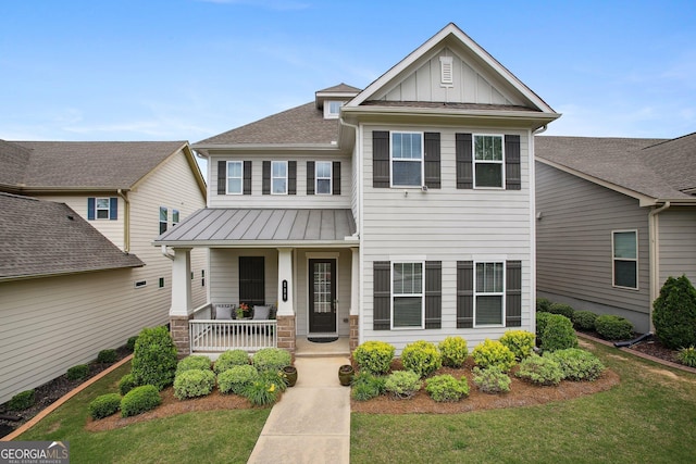 craftsman-style home with covered porch, board and batten siding, a standing seam roof, a front yard, and roof with shingles
