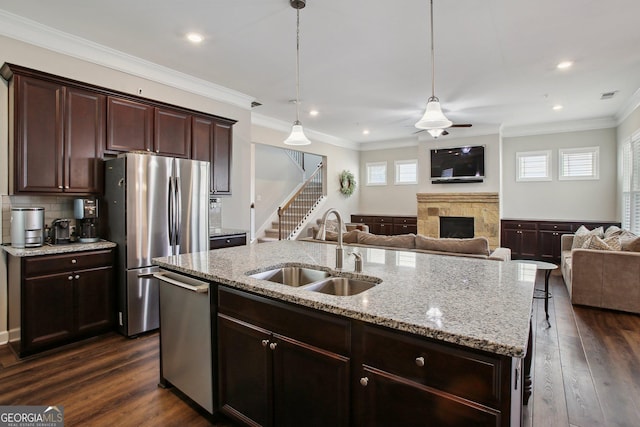 kitchen with a stone fireplace, open floor plan, a center island with sink, a sink, and stainless steel appliances