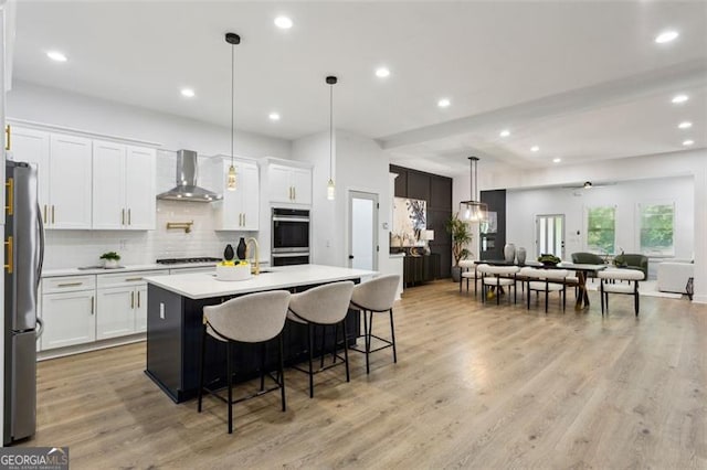 kitchen featuring white cabinets, appliances with stainless steel finishes, light countertops, wall chimney exhaust hood, and backsplash
