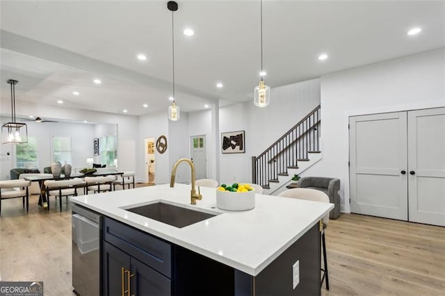 kitchen featuring stainless steel dishwasher, open floor plan, a sink, and light wood-type flooring