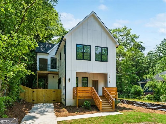 view of front facade with board and batten siding, fence, a gate, and a balcony