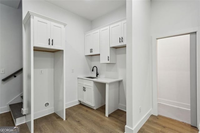 kitchen featuring light wood-type flooring, a sink, light countertops, white cabinets, and baseboards